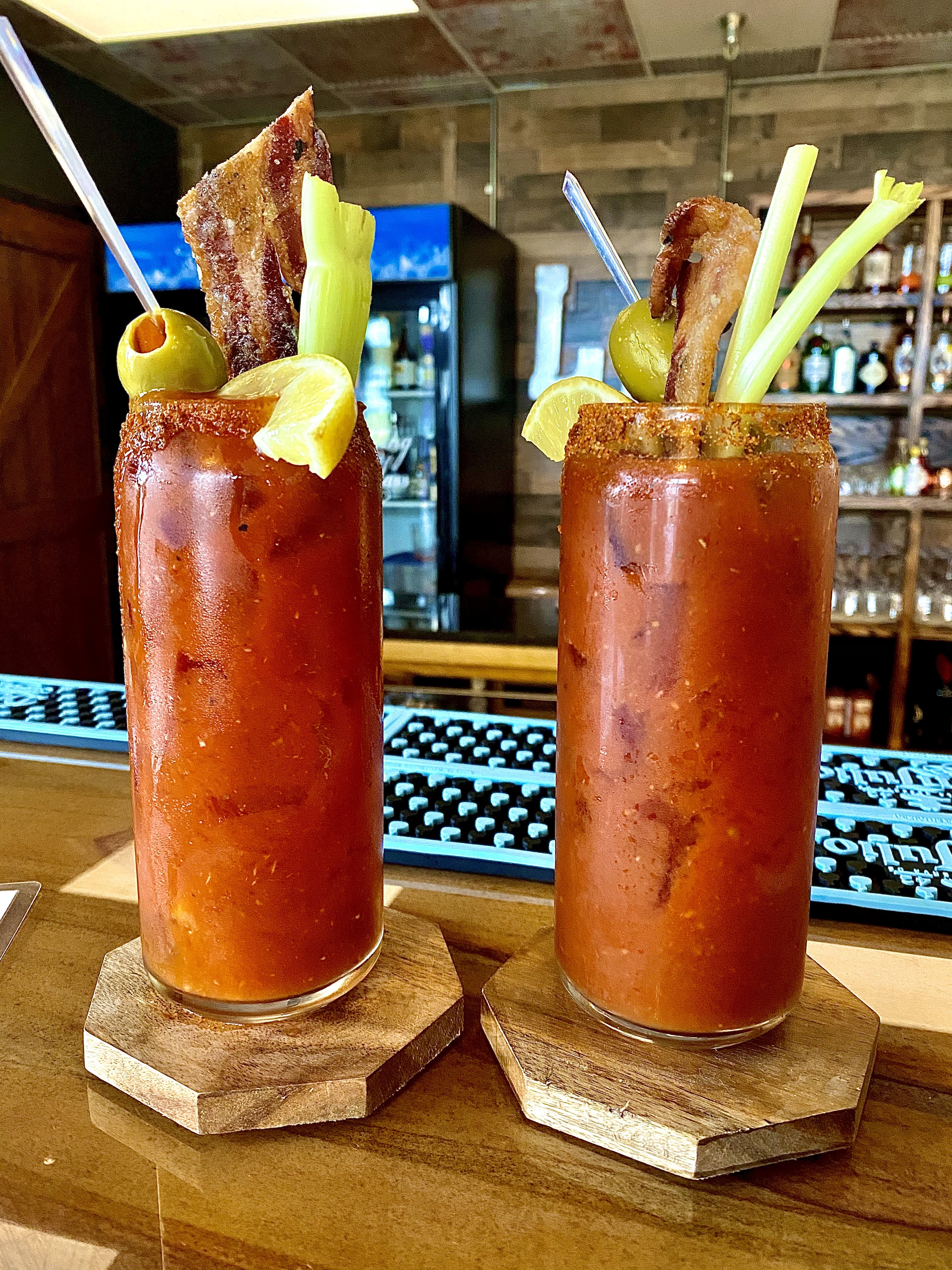 2 GEORGE’S® Bacon Infused OLD BAY® Bloody Marys served in OLD BAY® rimmed glasses with bacon and OLD BAY® seasoned celery stalk garnish