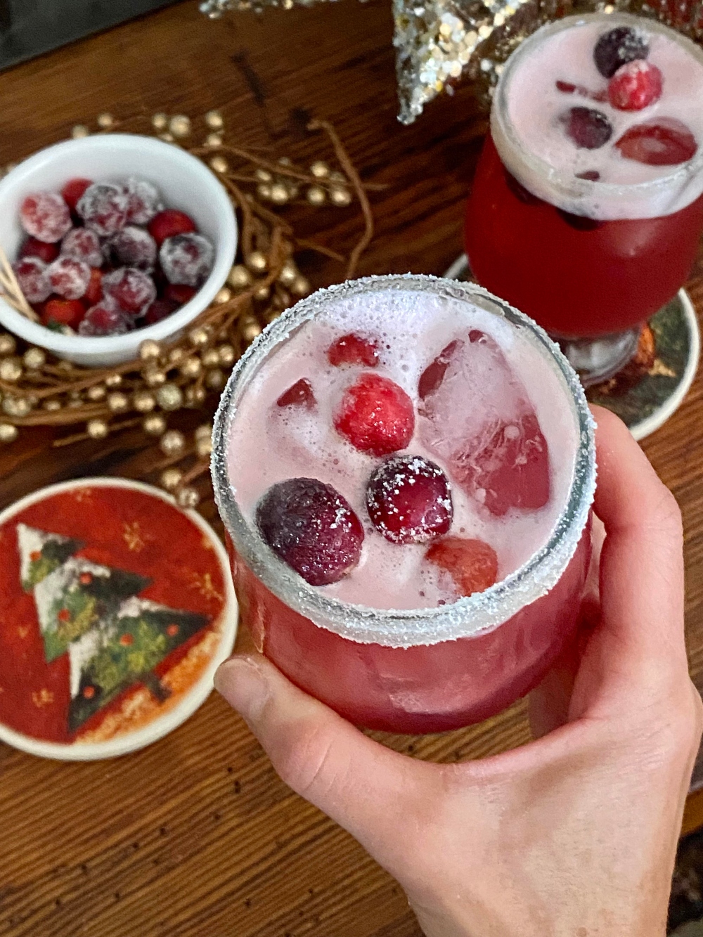 hand holding cocktail with cranberries with christmas theme
