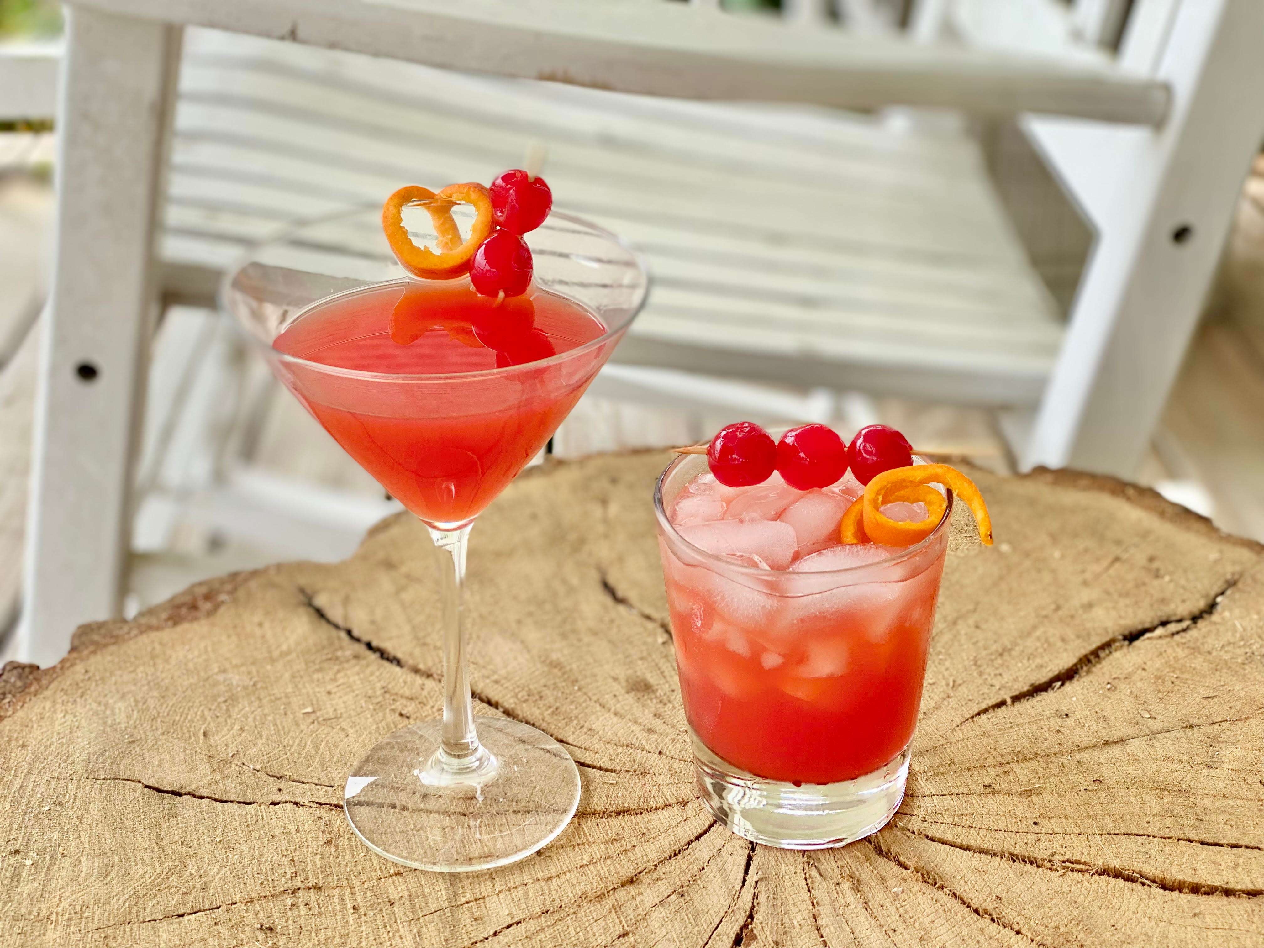 two cocktails with orange rinds and cherries on wooden table
