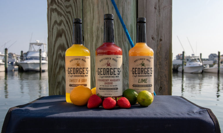 GEORGE’S® Craft Cocktail Mixes served with limes, lemons, and strawberries on table on marina dock