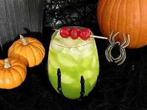 george's witches brew in a spooky wine glass with pumpkins next to it